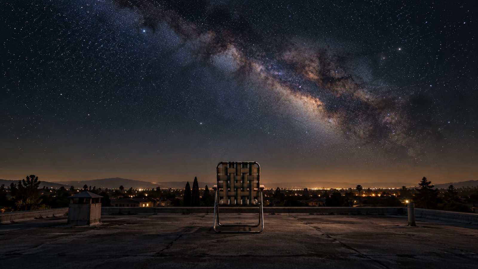 Cadeira de praia solitária no telhado de uma casa de subúrbio à noite, sob um céu imenso e estrelado, com a Via Láctea atravessando o alto e o brilho fraco de uma cidade distante